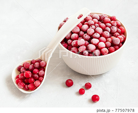 Frozen cranberries in a bowl with a spoon on a white background close-up. Red berries with hoarfrost. Frozen food. Side view. 77507978