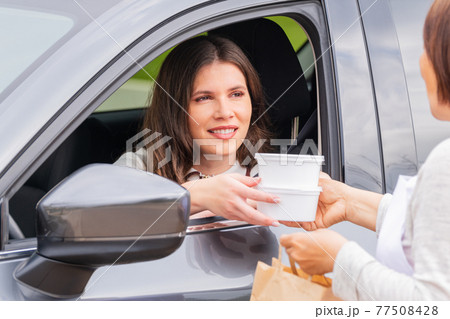 Woman in a car grabbing takeaway food containers 77508428