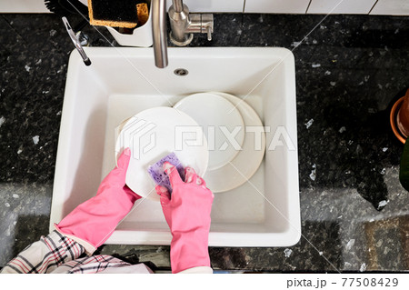 top view on female hands in gloves rinsing dishes with purple sponge above kitchen sink top view on female hands in gloves rinsing dishes with purple sponge above kitchen sink 77508429