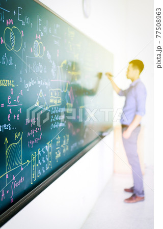 Businessman tries to solve math equation on black board 77508963