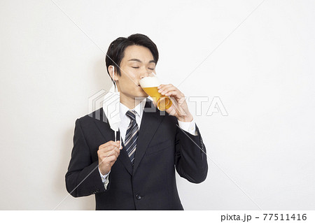 マスクを外して目を閉じてビールを飲む男性 77511416