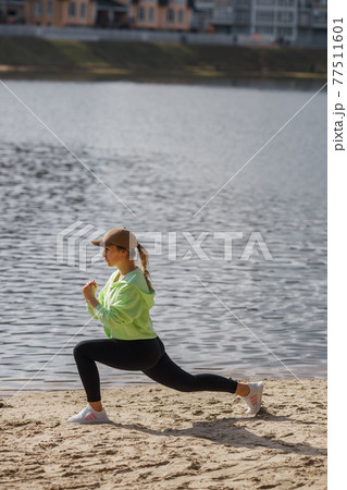 Veautiful self determied female runner in trendy sportswear posing isolated on river bank, stretching legs, warming up muscles before running exercise outdoors early in the morning Veautiful self determied female runner in trendy sportswear posing isolated on river bank, stretching legs, warming up muscles before running exercise outdoors early in the morning 77511601