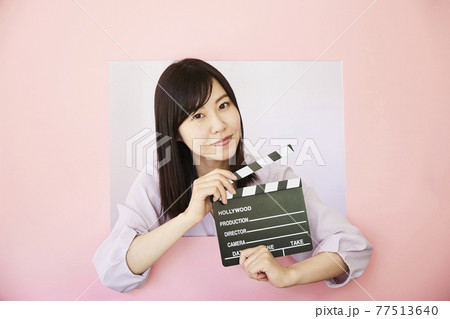 Woman holding clapperboard on pastel pink colored Woman holding clapperboard on pastel pink colored 77513640