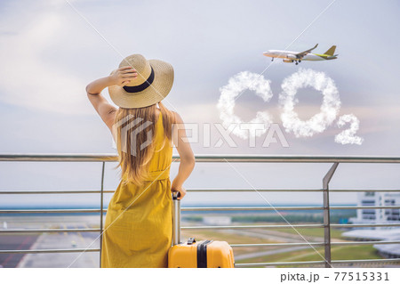 Beautiful young woman ltraveler in a yellow dress and a yellow suitcase is waiting for her flight CO2 lettering made of clouds. Sky with CO2 pollution, smog 77515331