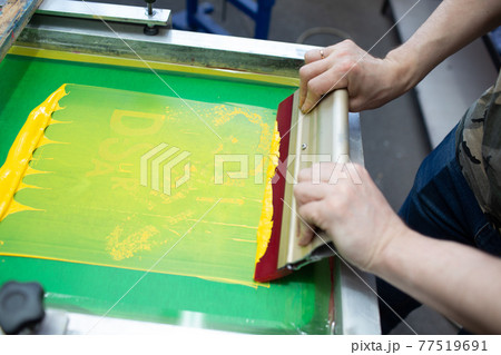 Serigraphy silk screen print process at clothes factory. Frame, squeegee and plastisol color paints Serigraphy silk screen print process at clothes factory. Frame, squeegee and plastisol color paints 77519691