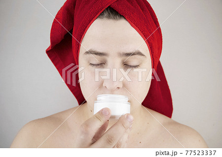 Funny man with a red towel on his head sniffs, tastes and smears a cream on his face. The concept of male self-care, spa treatments and male cosmetics Funny man with a red towel on his head sniffs, tastes and smears a cream on his face. The concept of male self-care, spa treatments and male cosmetics 77523337