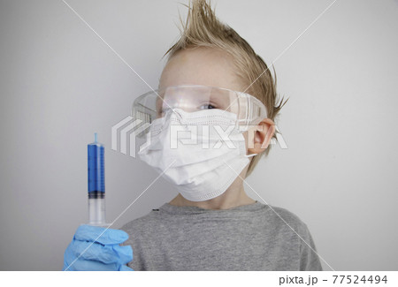 The child plays a doctor and a scientist. A boy in a medical mask studies a medicine in a test tube through a magnifying glass. The concept of education and promotion of medical professions The child plays a doctor and a scientist. A boy in a medical mask studies a medicine in a test tube through a magnifying glass. The concept of education and promotion of medical professions 77524494