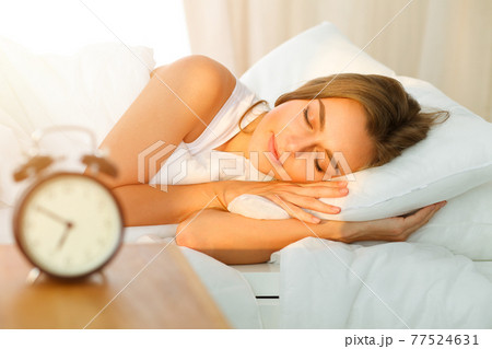 Beautiful blonde girl sleeping sweetly in sunny bedroom on a white bed. Holyday comfort and Rest concepts 77524631