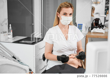 Female dentist at work with patient examining her teeth with dental tools 77526666