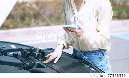 自動車のボンネットを開けてスマホを持つ女性　故障　ロードサービス 77528536