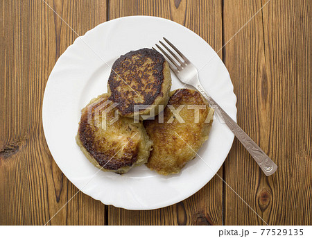 A plate with a Belarusian dish potato pancakes with meat filling. Wooden background, close-up A plate with a Belarusian dish potato pancakes with meat filling. Wooden background, close-up 77529135