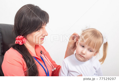 Doctor pediatric otolaryngologist examines the ear of a child of a little girl whose sulfur plug in the ear, background 77529207