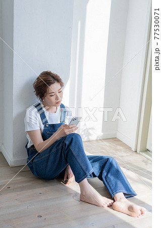 ジェンダーレス Lgbt 男の子みたいな女の子 オーバーオールを着て床に座ってスマホを触る若い女性の写真素材
