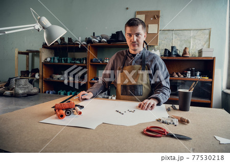 In a family shoe shop a young apprentice works with paper to create a pattern for shoes 77530218