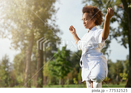 Serene Afro American girl in kimono meditating outdoors Serene Afro American girl in kimono meditating outdoors 77532525