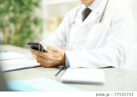 Doctor sitting at the table and using modern smartphone 77532735