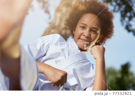 Cheerful Afro American girl practicing martial arts outdoors 77532921