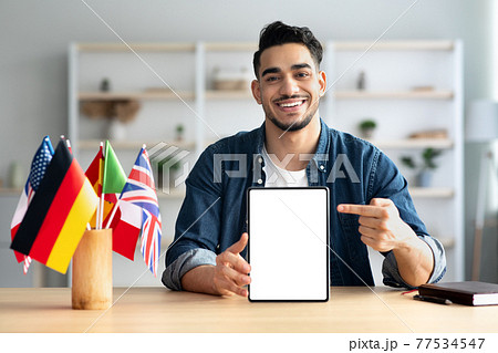 Cheerful arab guy pointing at digital tablet with empty screen Cheerful arab guy pointing at digital tablet with empty screen 77534547