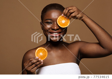 Fruit Acid Peel. Portrait of happy black lady holding two orange slices Fruit Acid Peel. Portrait of happy black lady holding two orange slices 77534615