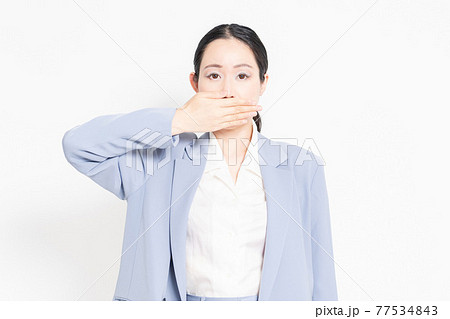 白バックの前に立って、口を隠すジェスチャーをする女性 77534843