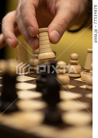 Hand taking next step on chess game. Human hand moving wooden white rook piece Hand taking next step on chess game. Human hand moving wooden white rook piece 77534876