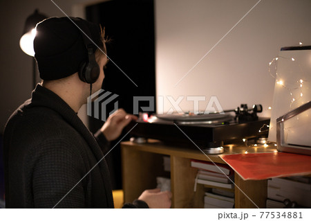 Young unshaven handsome hipster guy push start button on turntable backlit Young unshaven handsome hipster guy push start button on turntable backlit 77534881