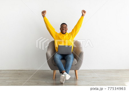 Joyful African Guy With Laptop Shaking Fists Over Gray Wall 77534963