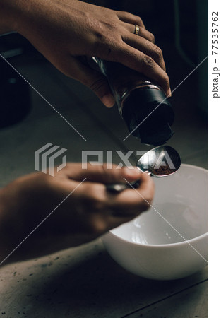 Measuring instant coffee powder into a bowl, holding the spoon by women's hand. Preparing to whisk into foam to make Dalgona coffee. 77535762
