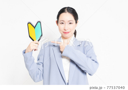 白バックの前に立って、初心者マークを持っている女性 白バックの前に立って、初心者マークを持っている女性 77537040