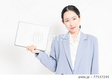 白バックの前に立って、小さいスケッチブックを持つ女性 77537295
