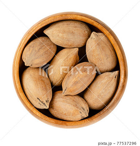 Unshelled pecan nuts, in a wooden bowl. Whole pecans, seeds and edible nuts of Carya illinoinensis. Used as a snack and in various recipes. Close-up, from above, isolated over white, macro food photo. 77537296