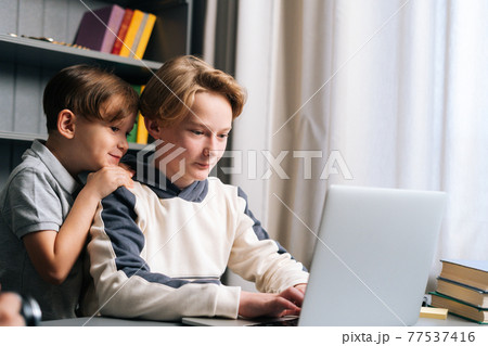 Close-up view of two young little brother watching video on laptop sitting at desk in cozy children room at home. 77537416