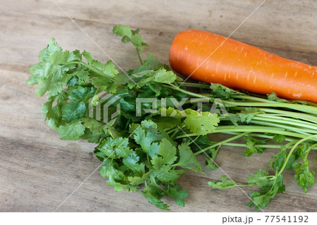 Green coriander and orange carrot on wooden background 77541192