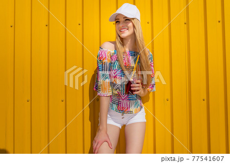 Pretty young hipster style girl have fun outdoor in white cap and eating ice cream on yellow background urban style Pretty young hipster style girl have fun outdoor in white cap and eating ice cream on yellow background urban style 77541607