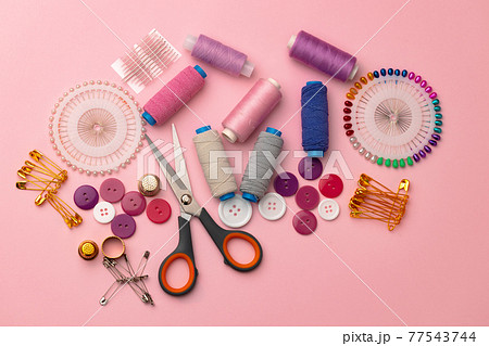Sewing accessories including thread spools and pins on pink background 77543744