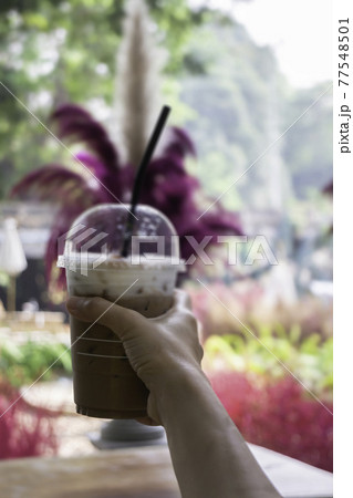 Iced coffee in her hand with garden background Iced coffee in her hand with garden background 77548501