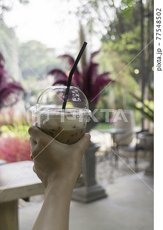 Iced coffee in her hand with garden background Iced coffee in her hand with garden background 77548502