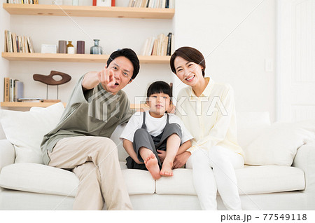 ソファーに座ってテレビ画面を指さす親子3人ファミリー ソファーに座ってテレビ画面を指さす親子3人ファミリー 77549118