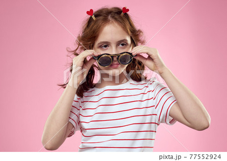 Cheerful little girl in fashionable glasses hairstyle decoration striped t-shirt pink background 77552924