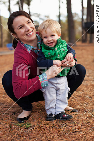Laughing mother tickling son in park 77554999