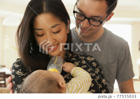 Mother feeding baby daughter whilst father watches 77555033