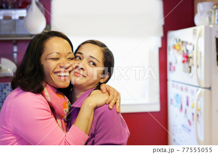 Portrait of mother hugging daughter in kitchen Portrait of mother hugging daughter in kitchen 77555055