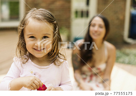Portrait of female toddler with mother blowing bubbles in garden Portrait of female toddler with mother blowing bubbles in garden 77555175