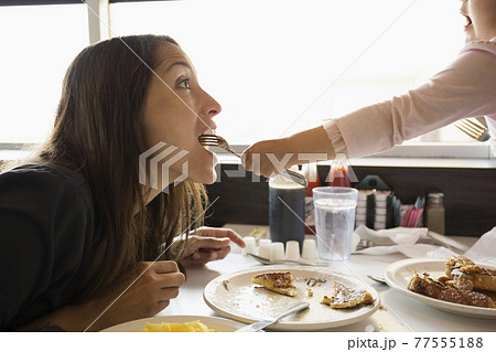 Toddler daughter feeding mother from fork in diner Toddler daughter feeding mother from fork in diner 77555188