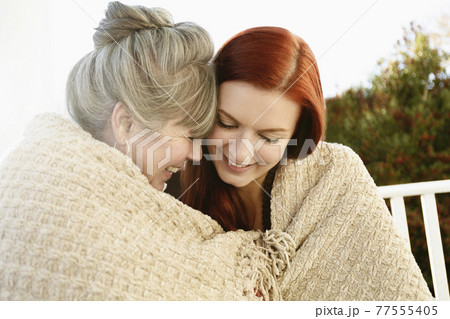 Senior woman and adult daughter face to face wrapped in a blanket on porch Senior woman and adult daughter face to face wrapped in a blanket on porch 77555405