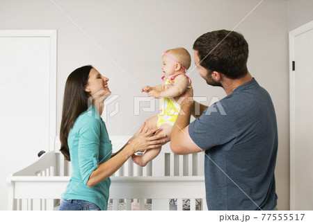 Mid adult couple holding up baby daughter in nursery 77555517