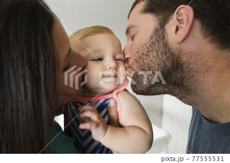 Close up of mid adult couple kissing baby daughter on each cheek 77555531