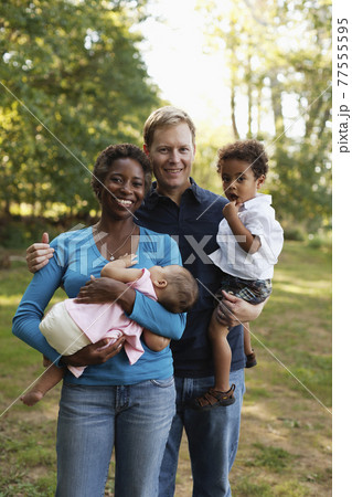 Family outdoors posing for photograph holding preschool boy and baby girl looking at camera smiling 77555595