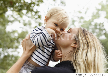 Mother kissing baby girl on cheek, outdoors 77555619