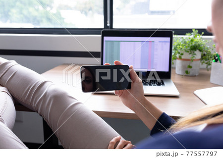 Caucasian businesswoman sitting at desk having video call conversation using smartphone Caucasian businesswoman sitting at desk having video call conversation using smartphone 77557797